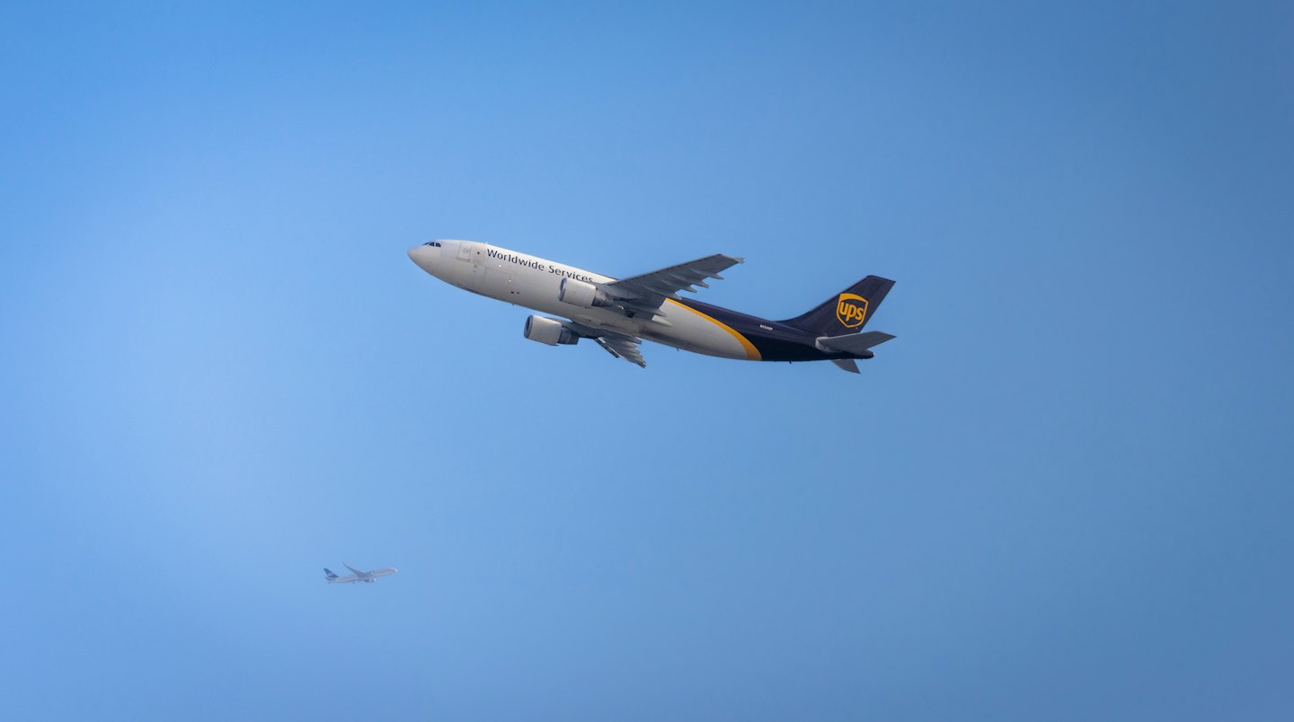 A large UPS cargo plane flies through the clear sky.